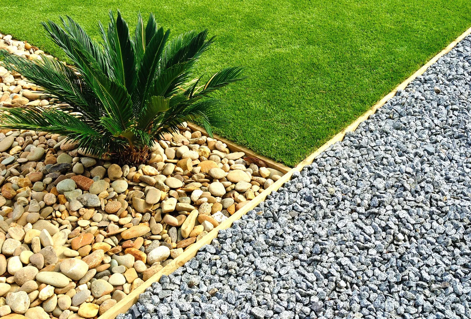 Mowed lawn meeting a river-rock bed and a section of gray gravel