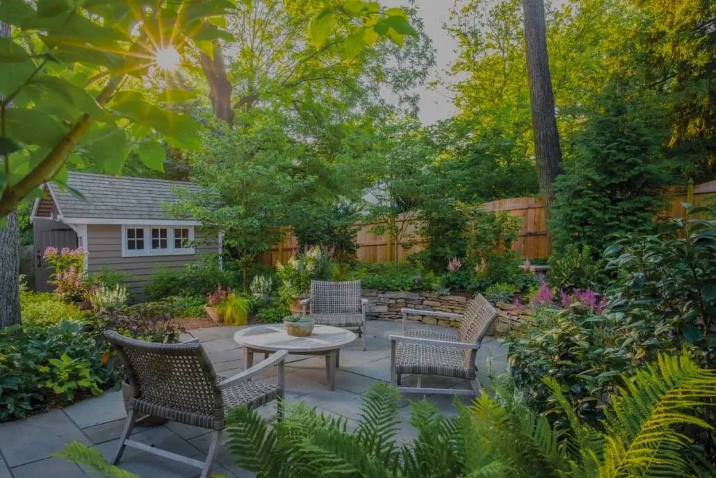 Backyard with a stone patio, planted beds, and a wooden fence